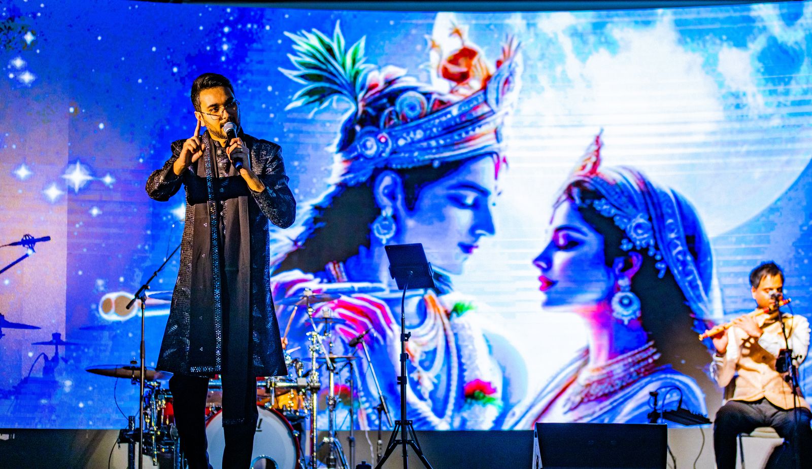Priyesh Shah talking to the audience in front of a moonlit Radha Krishna artwork