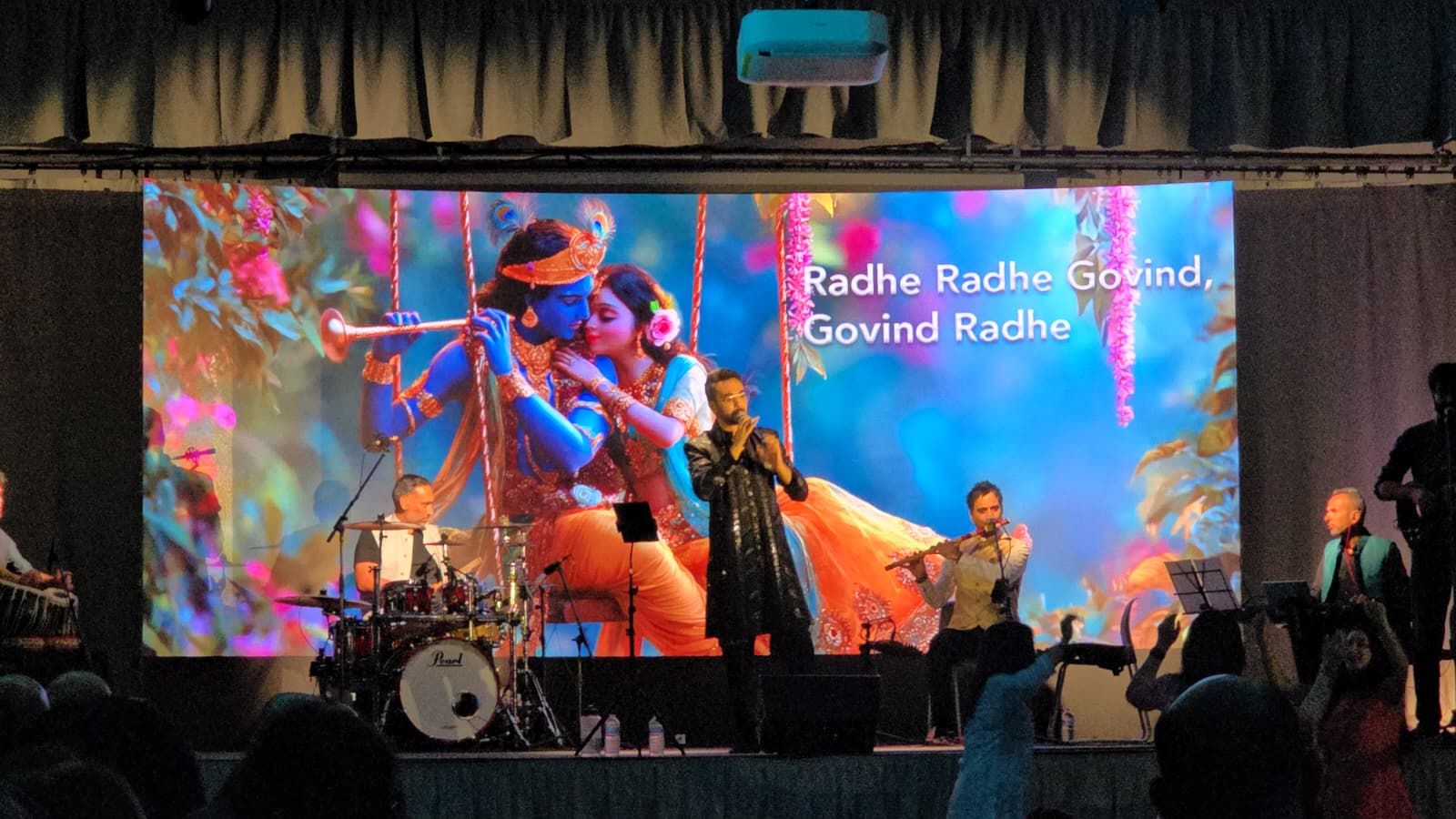 Audience members dancing at the front as the lyrics Radhe Radhe Govind appear on screen