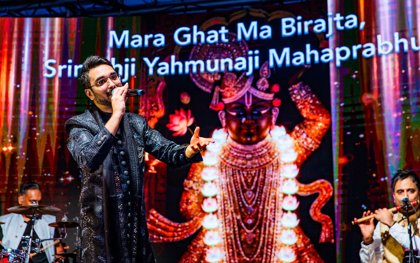 Priyesh Shah singing with Shrinathji on the screen behind him and the bansuri player to one side